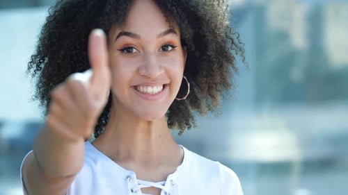 Glückliches fröhliches afroamerikanisches Mädchen mit Afro, zackiges Lächeln, zeigt ihren Daumen hoch, Geste des Brunnens