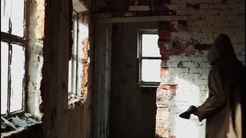 a Man in a Long Cloak with a Hood Walks in an Abandoned Building with Bloody Ax