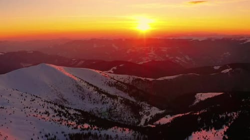 Volando sobre la montaña de invierno. Durante el amanecer o el atardecer. Cielo rojo y naranja.
