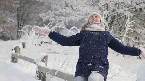 Glückliches Mädchen wirft Schnee mit erhobenen Händen in den Wald und lacht