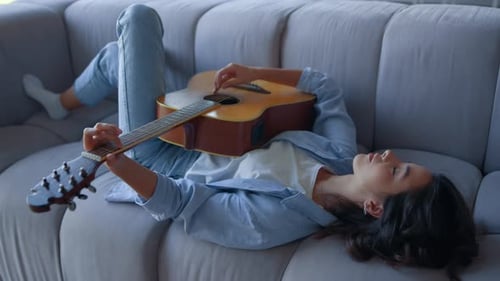 Young Woman Plays Guitar Lying on Couch