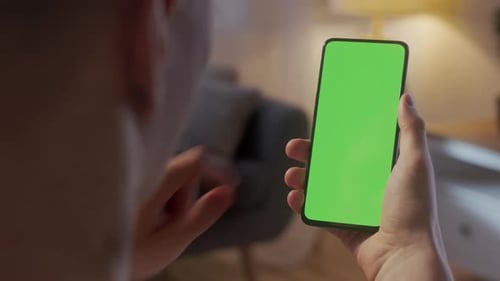 Handkamera Rückansicht des blonden Mannes mit Chroma-Key Greenscreen Smartphone beim Ansehen von Inhalten