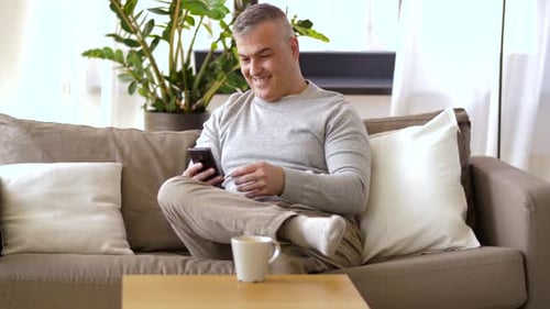 Man Using Smartphone and Drinking Coffee at Home