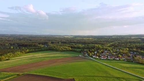 Wonderful spring day, flying forward smooth over a green field with a little village and a forest.