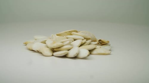 A Small Pile Of White Pumpkin Seeds Moving Slowly On The Turntable With Pure White Background - Cl