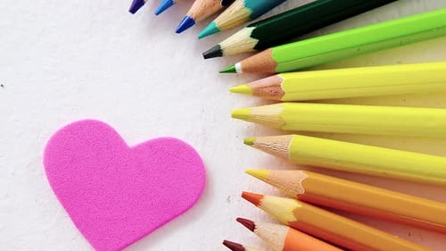Colored pencils arranged in semi circle with heart on white background