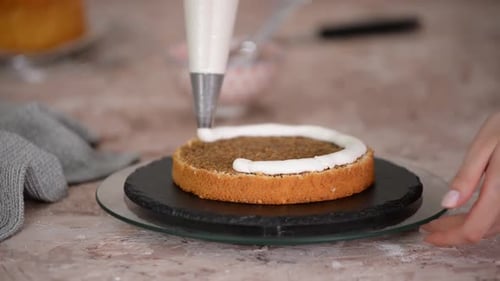 Nahaufnahme einer Frau, die Schlagsahne auf Schichtkuchen aufträgt.
