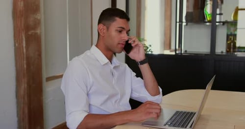 Young Man Talking on Phone While Working on Laptop