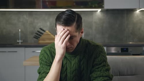Distraught Man in Kitchen Covers Face with Hand