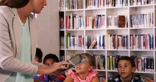 Teacher teaching school kids on digital tablet in library