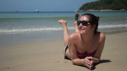 Mädchen liegt am Sandstrand und genießt Urlaub gegen Wellensurfer