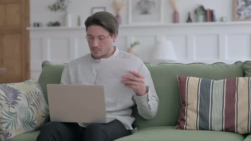 Man Reviews Paperwork on Laptop at Home