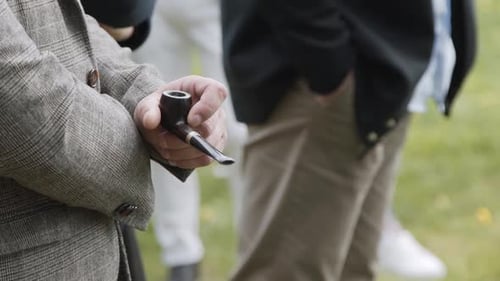 Mann im Business-Anzug steht auf Rasen und hält hölzerne Pfeife in der Hand