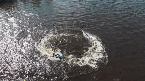 Ein Mann, der über dem Wasser herumfliegt, und ein anderer Mann, der Jetski im Kreis reitet