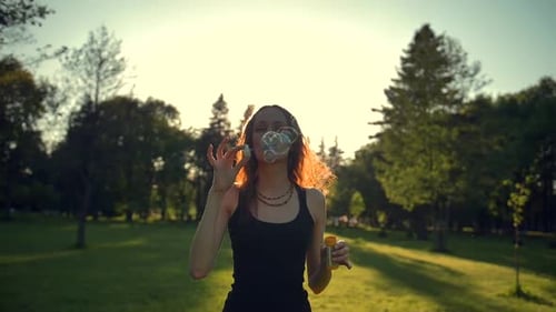 Woman Blowing Bubbles in a Sunny Park at Sunset
