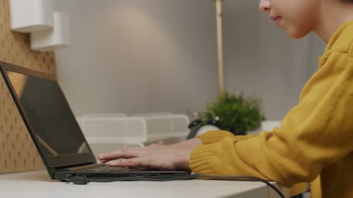 Young Adult Typing on Laptop at Desk