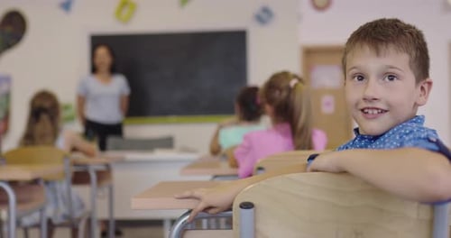 A Happy Boy Siting in a School Desk During the Class and Looking at the Camera