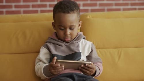 Child Plays With Phone on Yellow Couch