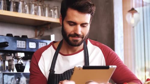 Smiling waiter using digital tablet at counter in cafe