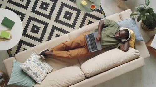 Man Relaxing on Couch Using Laptop and Headphones