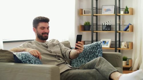 Man Video Calling on Phone While Relaxing on Couch