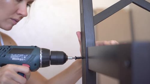 A Woman Is Assembling Furniture Using an Electric Screwdriver