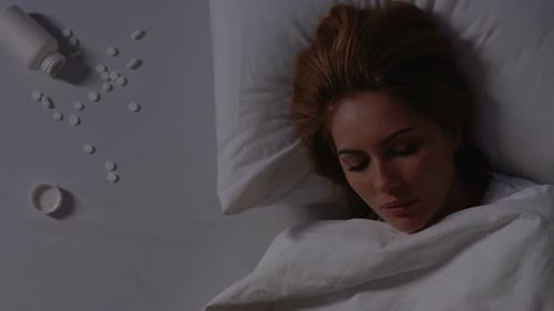 Woman Sleeps in Bed Near Scattered Pills