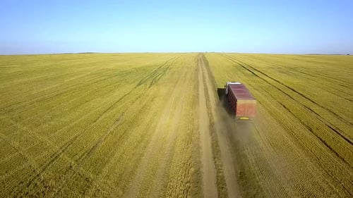 Aerial view of a truck driving on dirt road between plowed fields making lot of dust.