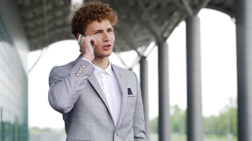 Salesman in Grey Suit Standing Outside Office Building Look Around While Talking on Mobile Phone