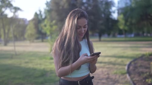 Young Woman Using Smartphone in Sunny City Park