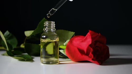 Dropper Releasing Liquid in Bottle Next to Rose