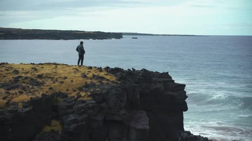 Man Stands on Cliff Overlooking Ocean