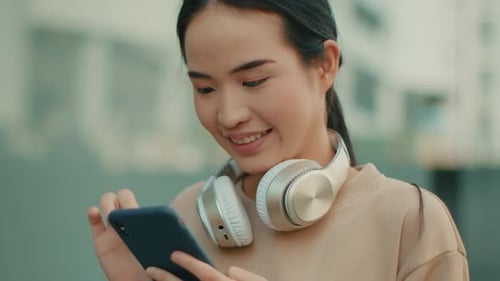 Portrait of Young Asian Woman in casual clothes using a smartphone standing at city street.