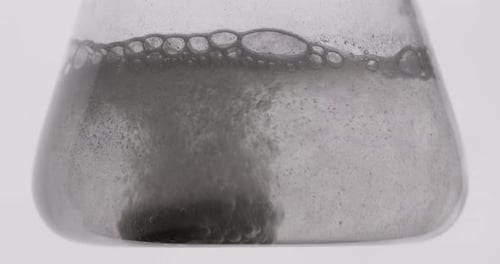 Prise de vue rapprochée. Un réactif est jeté dans un flacon rempli d'eau. Expériences en laboratoire.