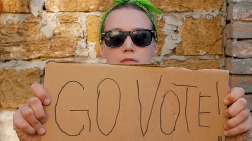 Woman shows cardboard with Go Vote sign brick wall urban background Voting concept Political choice