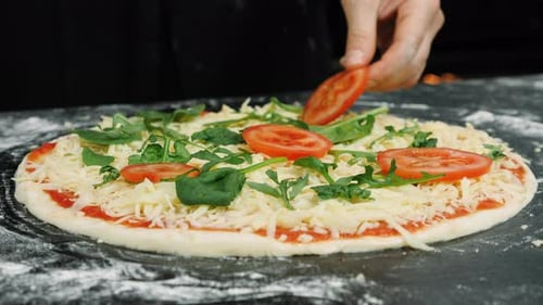 Hände legen Tomaten auf Pizzateig. Prozess der Zubereitung von Pizza