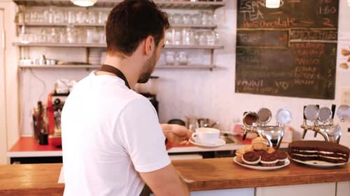 Friendly Bartender Cleaning Cafe Counter with Coffee and Muffins