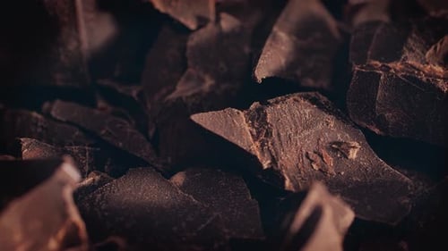 Chunks of sweet dark chocolate sliding backdrop, close-up. Gourmet dessert ingredient.