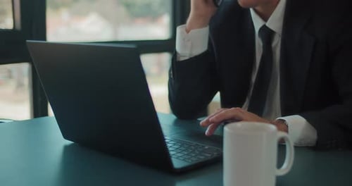 Close up of a businessman working on a laptop while holding a phone. Tracking shot, slow motion