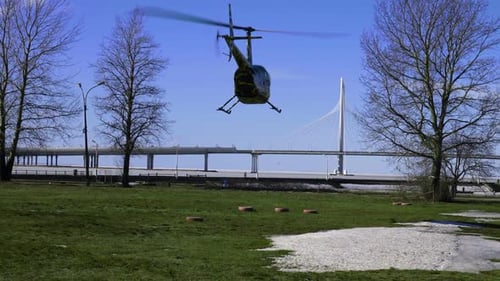 Camo Helicopter Parked on Grassy Field Near Bridge