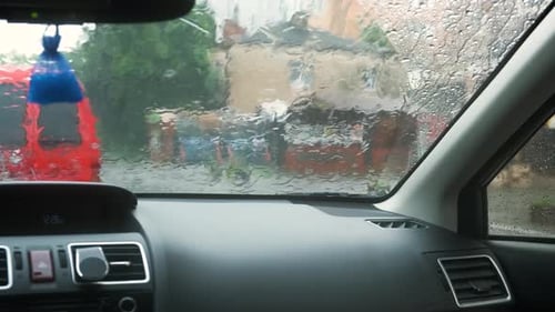 Close up view from inside of rain water drops falling on car windshield glass.