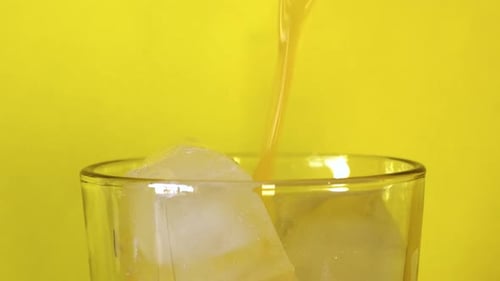 Pouring fresh orange juice into a glass with ice cubes. Close up shot.