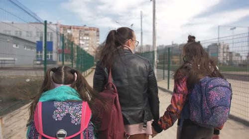 A Mother and Two Daughters in a Protective Antivirus Mask Walk Along the Street in an Isolated Area