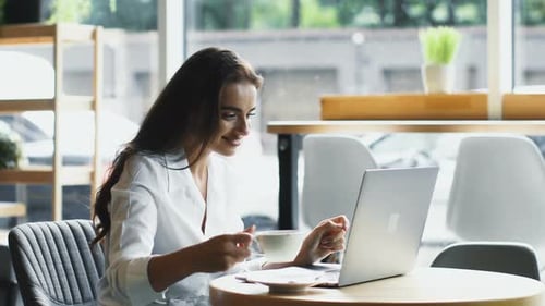 Woman Working on Laptop in Cafe, Drinking Coffee