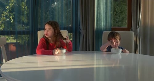 Brother and Sister Eating Breakfast at Table Indoors
