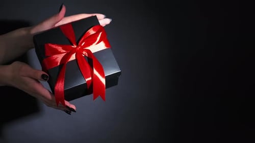 Woman Holds Black Gift Box with Red Ribbon
