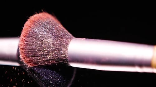 Schminkpinsel mit farbigem rotem Puderon auf schwarzem Hintergrund Zeitlupe