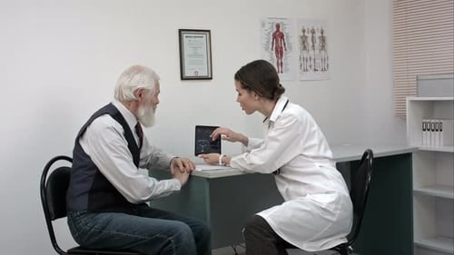 Woman Doctor Talking with Senior Patient in the Office and Showing Him Tablet with Mri