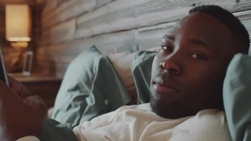 Man Lying in Bed Looking at Tablet
