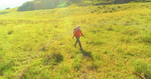 Flight Over Backpack Hiking Tourist Walking Across Green Mountain Field. Huge Rural Valley at Summer